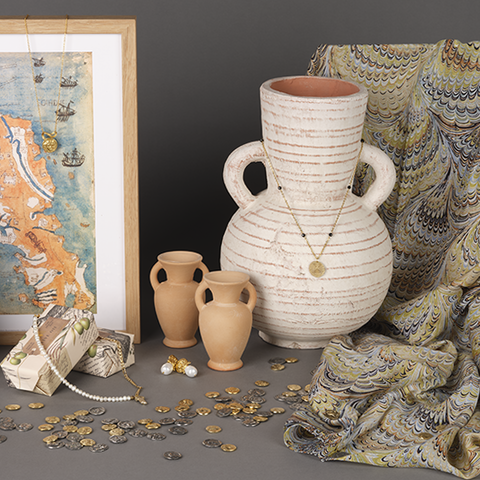 Range of Labyrinth shop products including gold jewellery, exhibition prints in frames, gold and silver coloured coins, olive oil soap, and a marbled green print silk scarf.