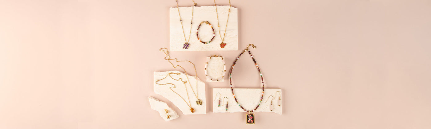 Six pieces of jewellery from the Ashmolean's Labyrinth range are displayed on a black cushion and a blue and white Temple design scarf. The collection of necklaces and earrings are gold, with a mixture of coin, pearl or column details.