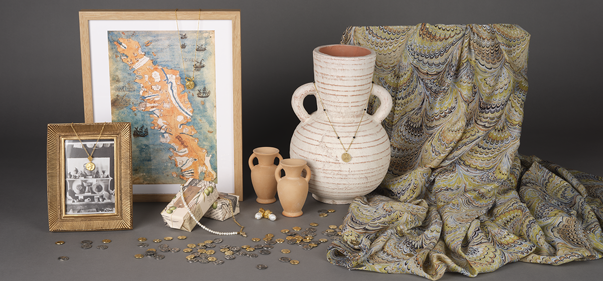 Range of Labyrinth shop products including gold jewellery, exhibition prints in frames, gold and silver coloured coins, olive oil soap, and a marbled green print silk scarf.