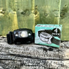 Outdoor display of a black head torch resting on tree trunk next to the item's green gift box with wooden fence background.