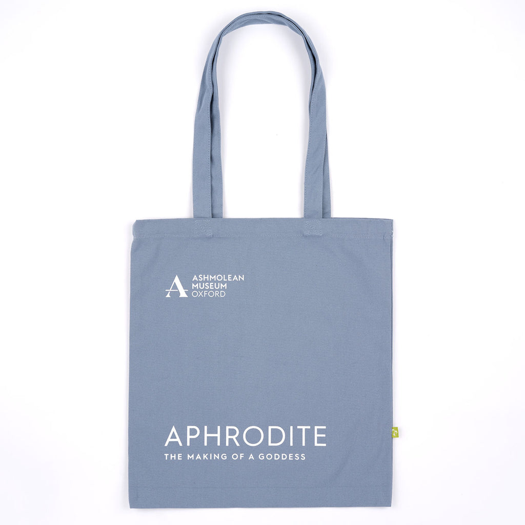 A slate blue canvas tote bag with white printed text reading 'ASHMOLEAN MUSEUM OXFORD' and 'APHRODITE THE MAKING OF A GODDESS'.