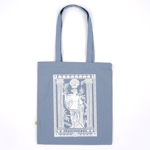 A slate blue canvas tote bag with long handles, featuring a large white graphic print of the Aphrodite statue on the front, set against a plain white background.
