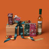 Gift box with festive items including a bottle of liqueur, jam jar, Christmas pudding, chocolate bars, and hamper box against an orange background