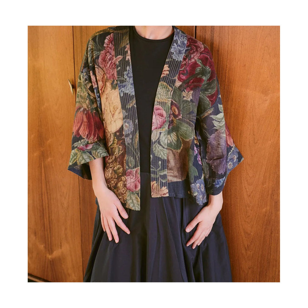 Person wearing a floral kimono over a black outfit against a wooden background