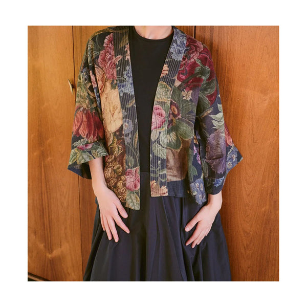 Person wearing a floral kimono over a black outfit against a wooden background