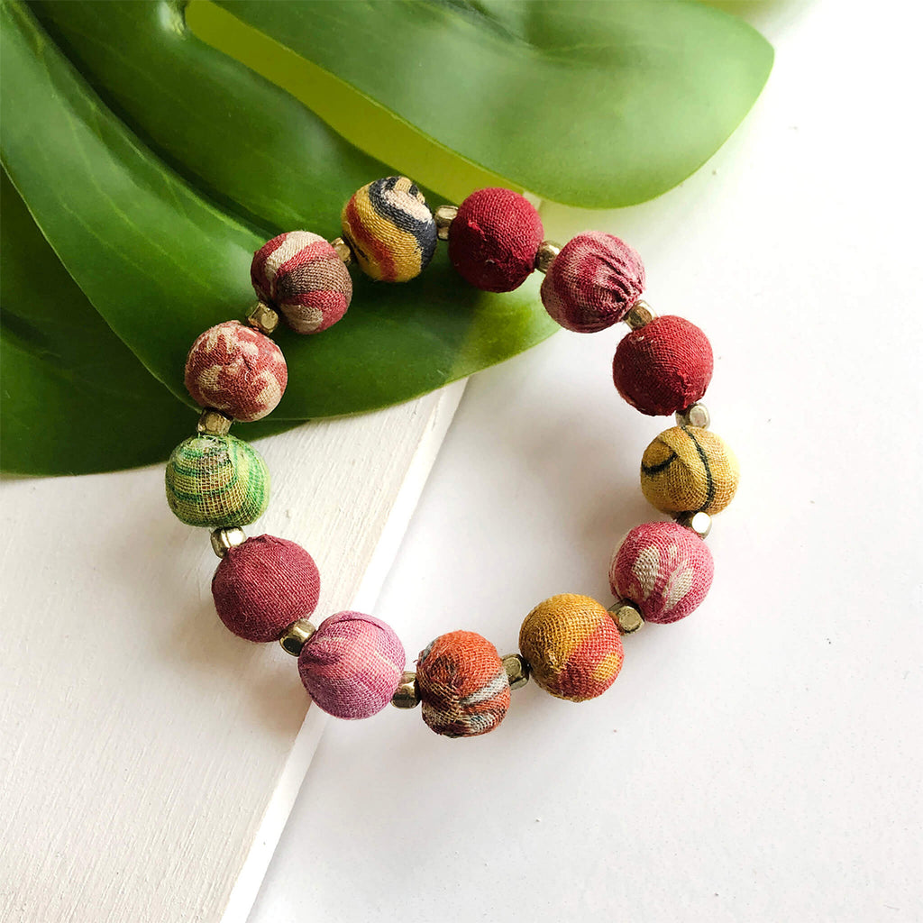 Multicolored beaded bracelet on a white surface with green leaves in the background