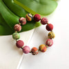 Multicolored beaded bracelet on a white surface with green leaves in the background