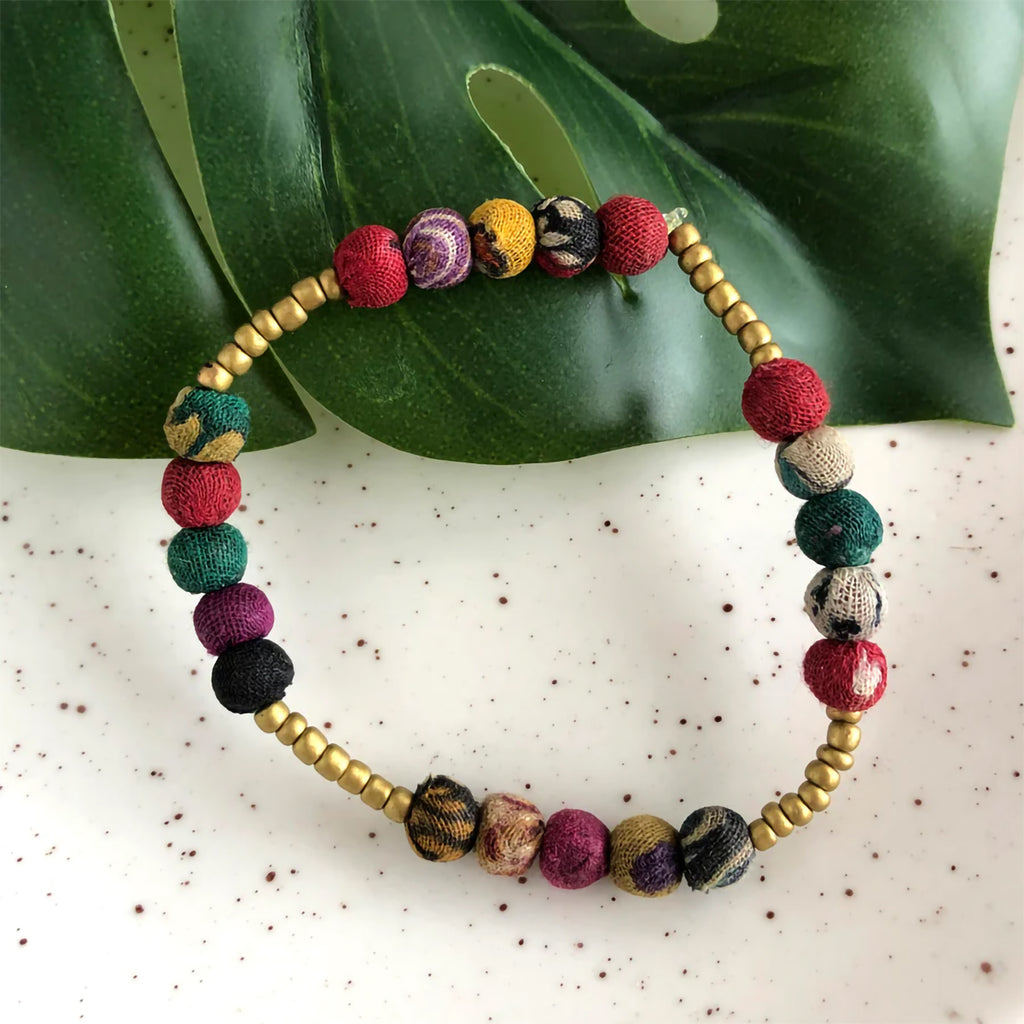 Colorful beaded bracelet with gold accents on a leafy background
