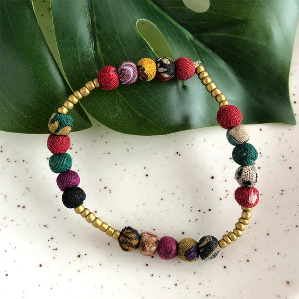 Colorful beaded bracelet with gold accents on a leafy background