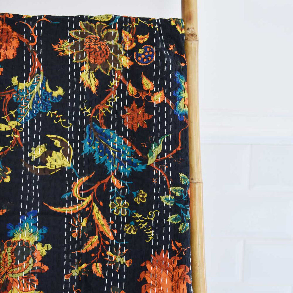Colourful floral patterned fabric throw with a dark autumnal colour palette draped over a bamboo stick on a white background