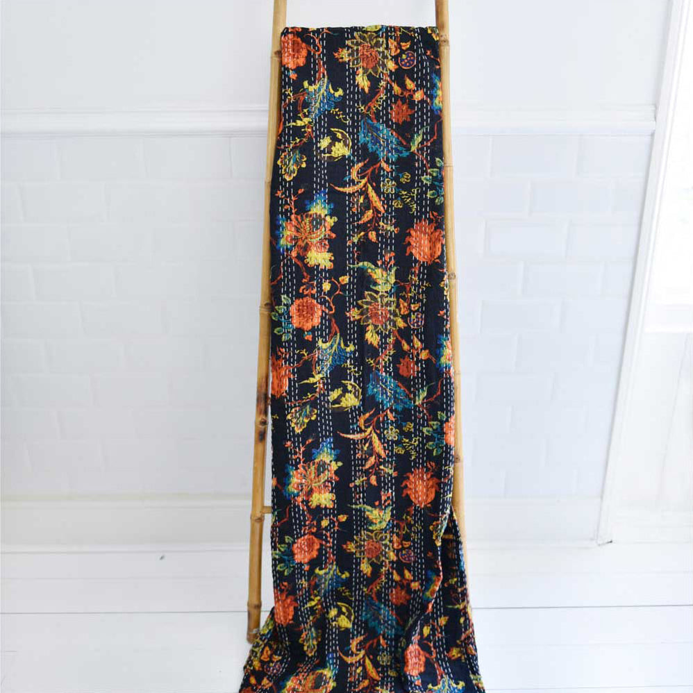 Floral patterned fabric throw with a dark background draped over a wooden ladder against a white background