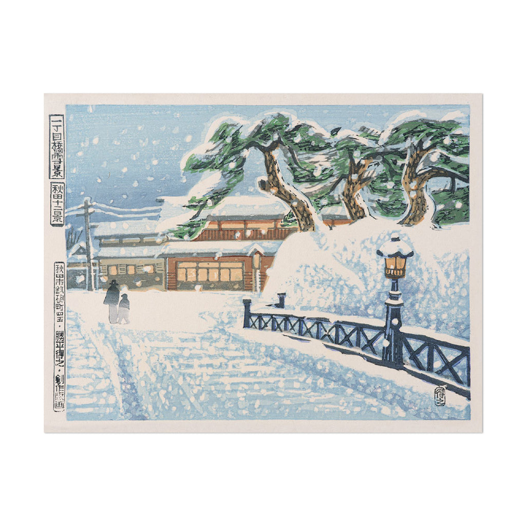 A square Japanese-style snow scene print with a light blue border. The artwork shows snow-covered trees, a snowy path, a bridge railing, a lamppost, and a small building with warm windows.