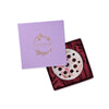 White ceramic halliesphere flower arranger with colourful may Morris poppy design inside of a purple square gift box with red velvet interior against a white background.