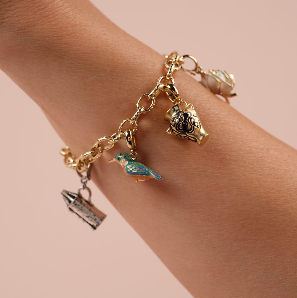 Gold charm bracelet on a wrist against a pink background