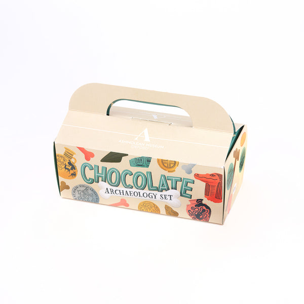 A cardboard gift box for a 'Chocolate Archaeology Set', featuring a cream-colored design with colourful illustrations of chocolate-themed artefacts and the text 'CHOCOLATE ARCHAEOLOGY SET' on a white background.