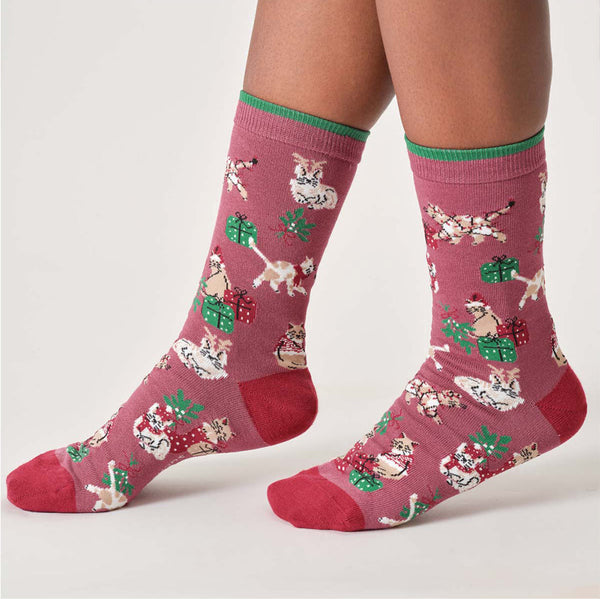 Pink socks with festive cat pattern worn by a person on a white background
