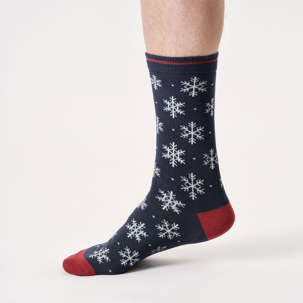 Navy sock with white snowflake pattern and red accents worn by a person on a light gray background