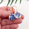 Gold hoop earrings with blue floral designs held in a hand against a white background