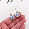 Earrings with blue floral design held between fingers on a white background