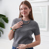 Woman wearing a gray sweater with colorful jewelry against a white wall.