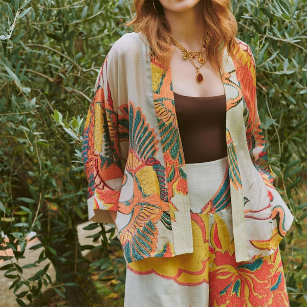 Person wearing a colorful kimono-style outfit with a patterned cardigan in a natural setting.