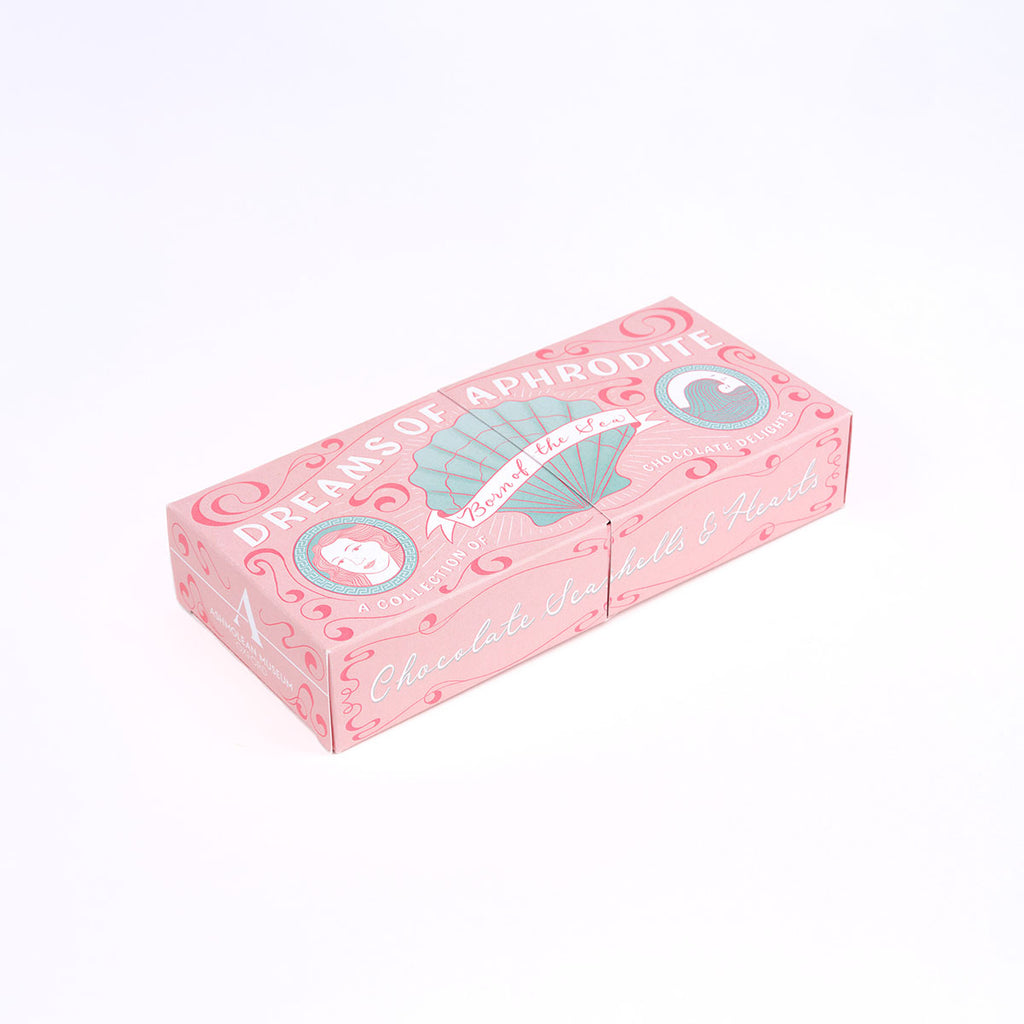 A pink decorative assorted chocolates box with illustrated shell and circular emblem graphics, photographed on a clean white background.