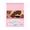 An open pink gift box filled with assorted chocolates on a white background. The box lid is pink and printed with the text 'DREAMS OF APHRODITE' and decorative shell artwork.