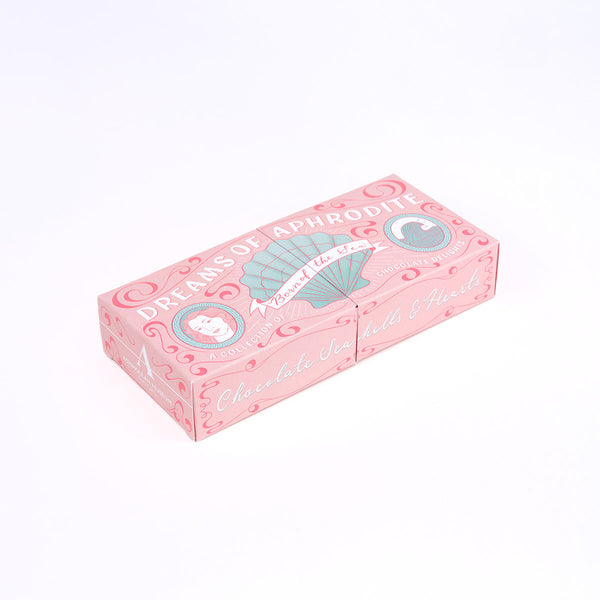 A pink decorative assorted chocolates box with illustrated shell and circular emblem graphics, photographed on a clean white background.