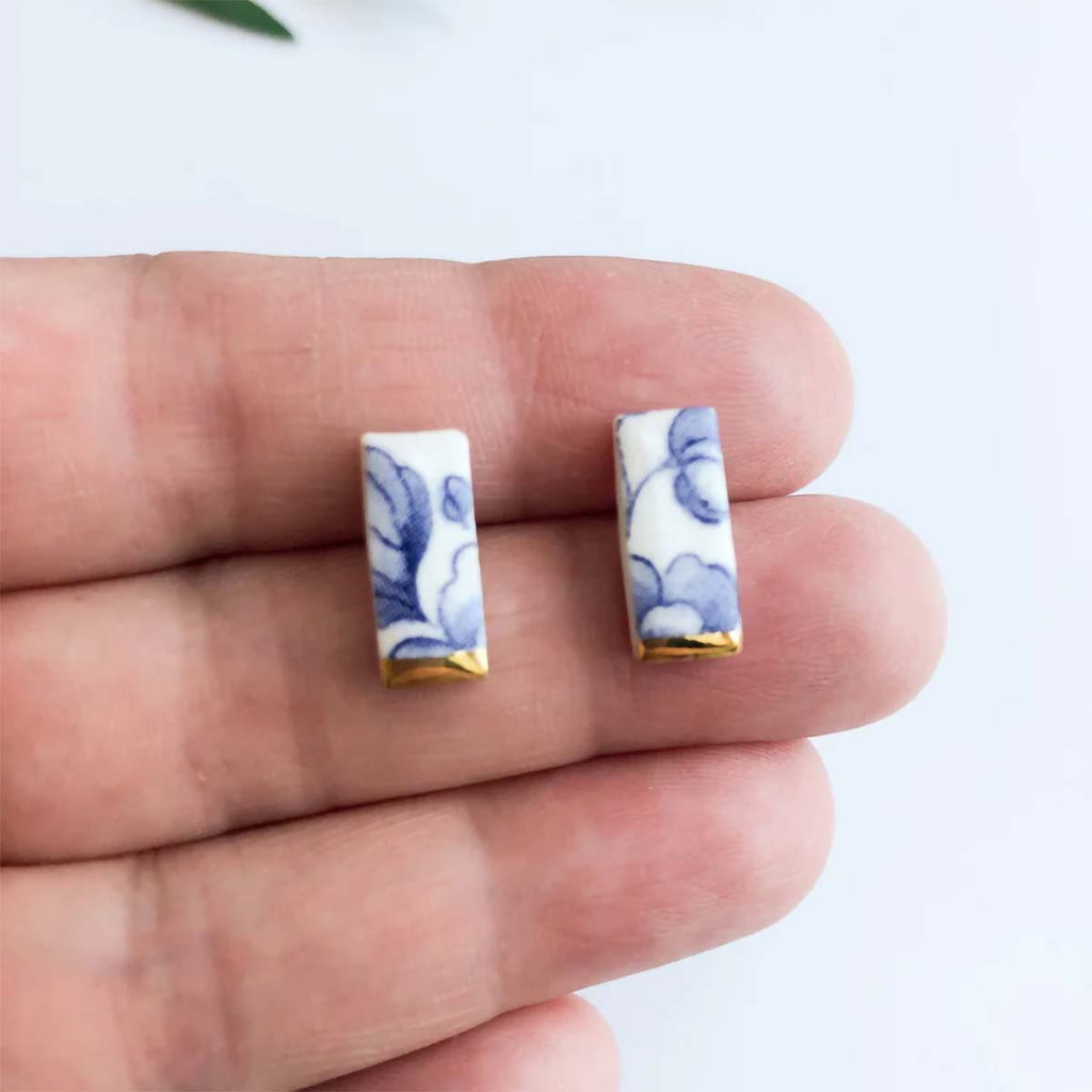 Rectangular earrings with floral design held between fingers on a white background
