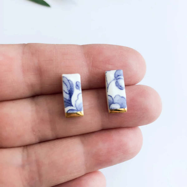 Rectangular earrings with floral design held between fingers on a white background