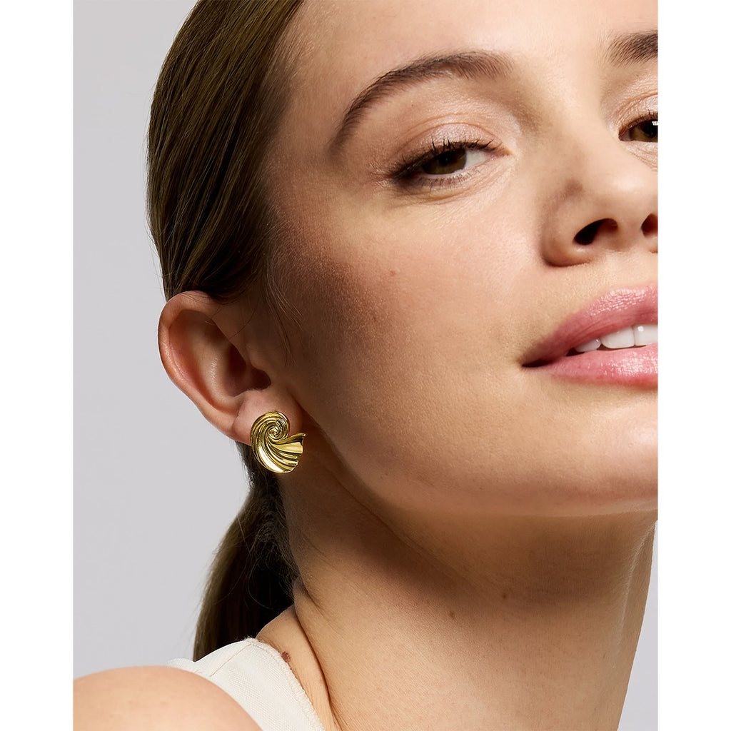 A close-up of a woman wearing a small gold crescent-shaped stud earring, shown from the side against a light gray background.