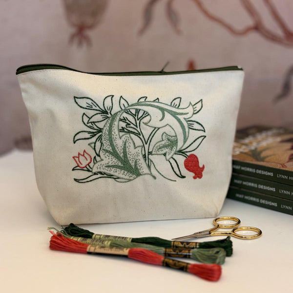 White pouch with green floral design, embroidery floss, and scissors on a white surface.