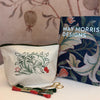 White pouch with May Morris floral design, embroidery book, and scissors on a patterned fabric background