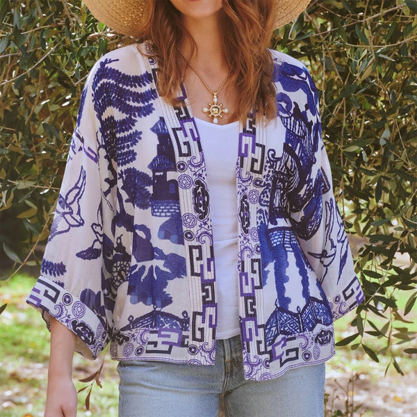 model wearing white and blue kimono jacket over jeans and t shirt in front of olive plants