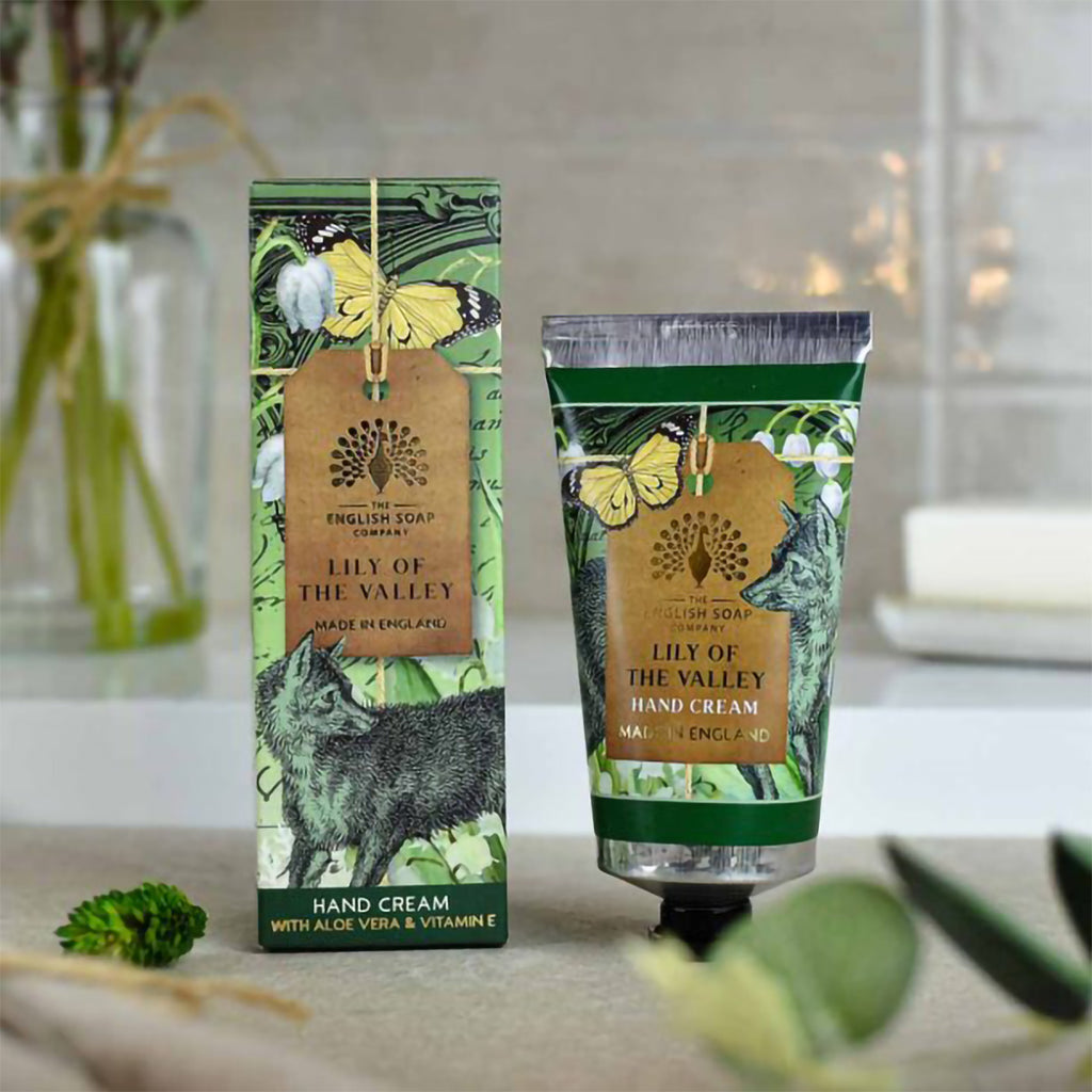 Lily of the Valley Anniversary hand cream displayed on table surrounded by green leaves in background.