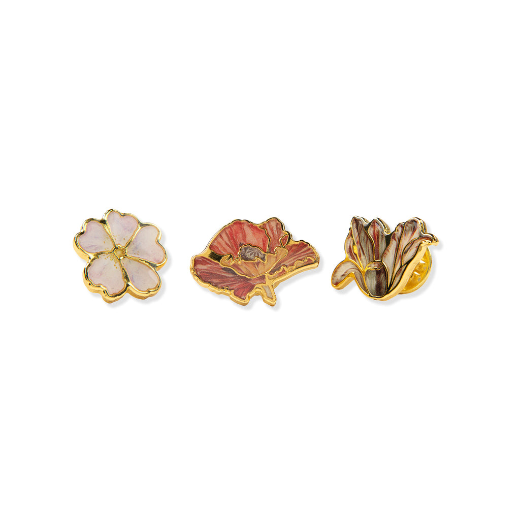 Three floral-shaped pin badges with gold accents on a white background