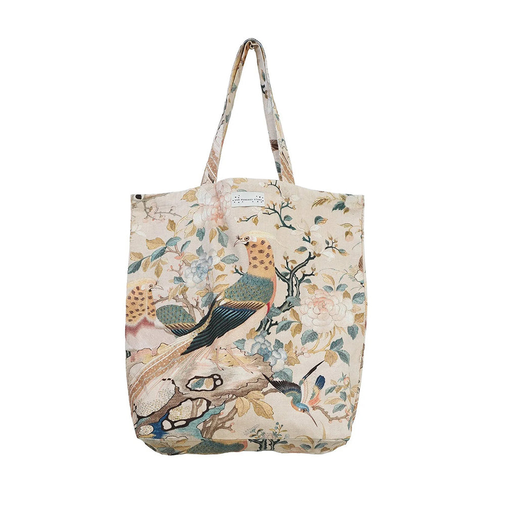 A canvas tote bag featuring a vintage-style botanical and bird print on a cream background, with two shoulder straps.