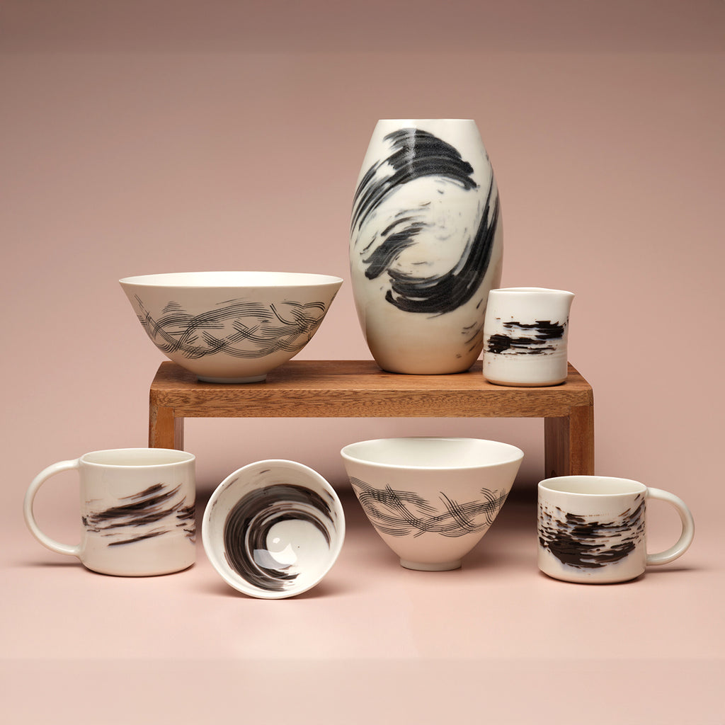 Set of white porcelain bowls and mugs with black abstract patterns against a pink background