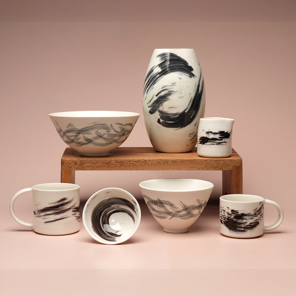 Set of white porcelain bowls and mugs with black abstract patterns against a pink background