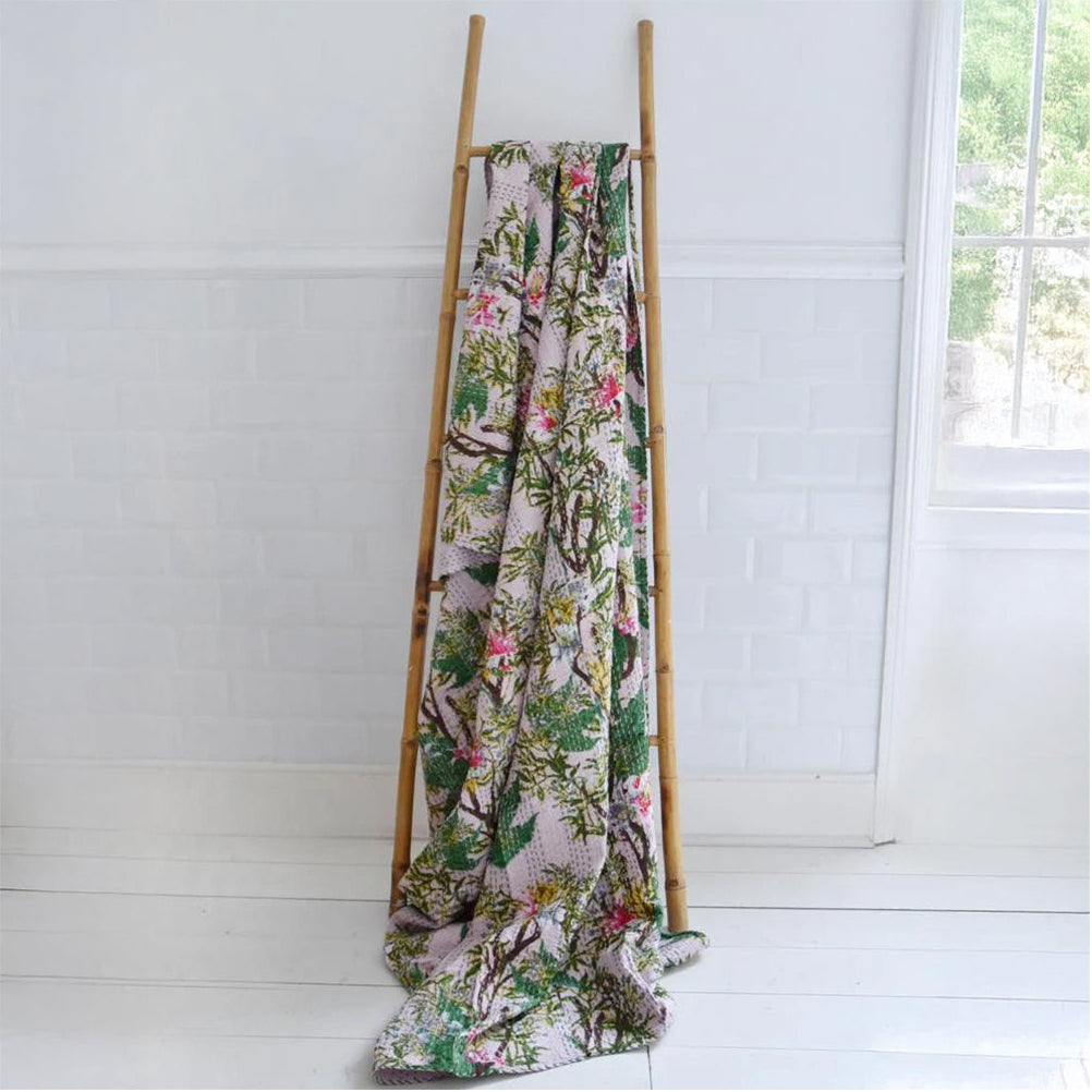 Floral-patterned blanket draped over a wooden ladder against a white wall.