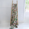 Floral-patterned blanket draped over a wooden ladder against a white wall.
