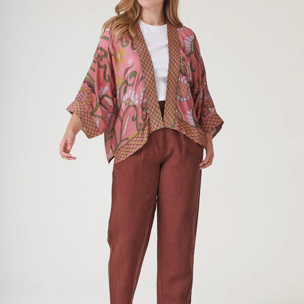 Model wearing pink and green floral Indian kantha kimono and brown trousers on a white background.