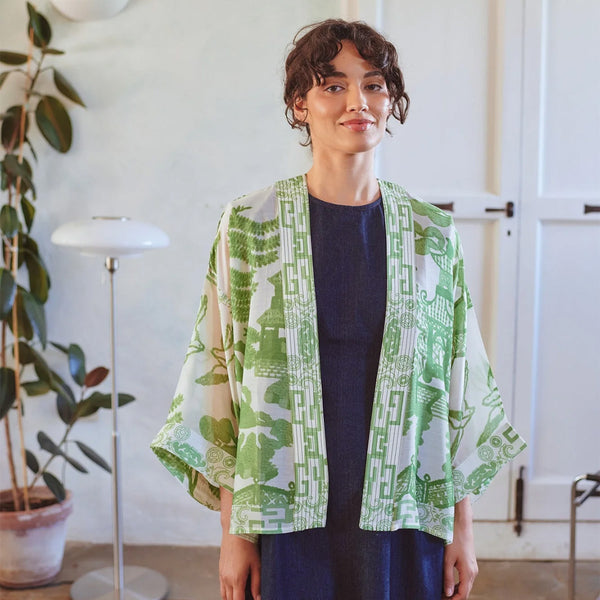 Woman wearing a green and white patterned kimono-style jacket indoors.