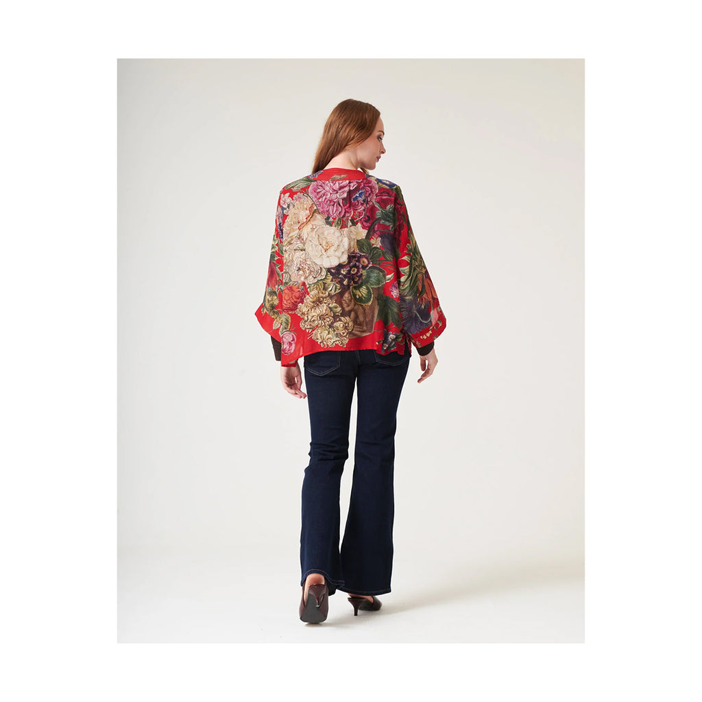 Woman wearing a colorful floral blouse and dark pants on a white background