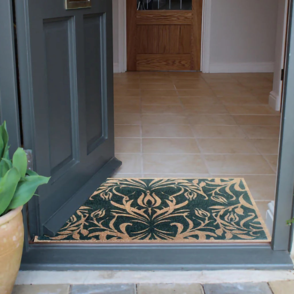 Lifestyle shot of green floor mat with May Morris floral design inside of home doorway. 
