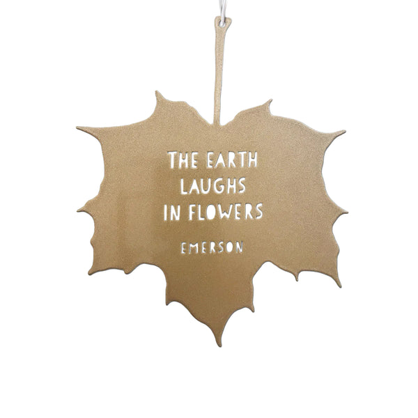 Decorative leaf-shaped sign with text by Emerson 'THE EARTH LAUGHS IN FLOWERS' on a white background
