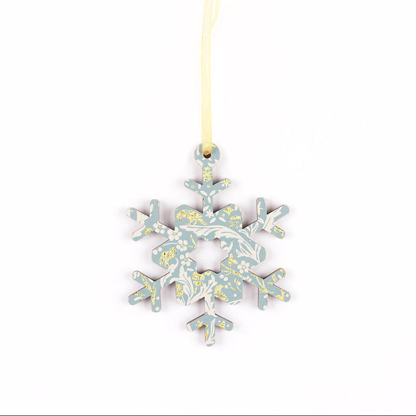 A decorative snowflake ornament with a light blue and white floral pattern and small gold accents, hanging from a pale gold ribbon on a white background.