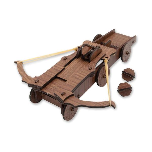 A wooden medieval crossbow toy with a dark brown wood-grain finish, light tan rubber bands, and two small loose wooden projectile components on a plain white background.
