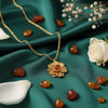 Gold necklace with a floral pendant on a green fabric background with amber stones and white flowers.