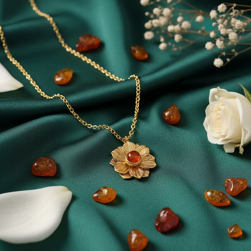 Gold necklace with a floral pendant on a green fabric background with amber stones and white flowers.